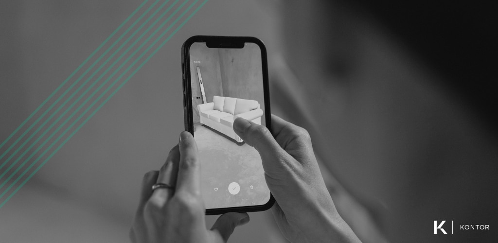 Black and white image of a person holding a smart phone using an AR application to visualize a new sofa in their home. Over the image are green diagonal lines. In the bottom right is the Kontor logo. 